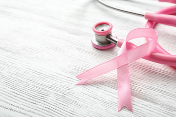 Pink ribbon and stethoscope on wooden background, space for text. Breast cancer concept