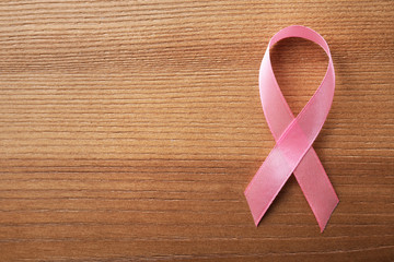 Pink ribbon on wooden background, top view with space for text. Breast cancer awareness concept