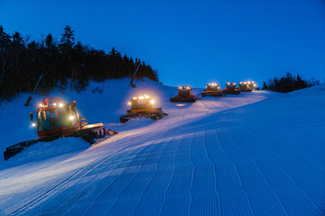 Fleet of snowcats grooming Spruce Peak at dusk, Stowe, Vermont, USA