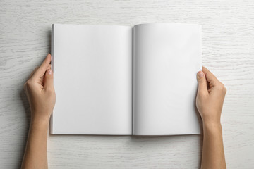 Woman holding brochure with blank pages on wooden background, top view. Mock up for design