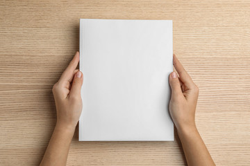 Woman holding brochure with blank cover on wooden background, top view. Mock up for design