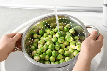 Woman washing fresh Brussels sprouts in colander, closeup