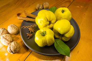 large yellow quince fruits on a ceramic plate, with anise, cinnamon, and walnuts