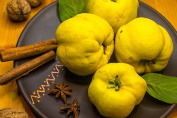 Naklejka na ściany i meble large yellow quince fruits on a ceramic plate, with anise, cinnamon, and walnuts