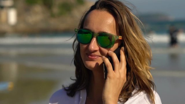 Happy, pretty woman talking on cellphone standing on beach