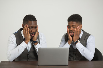 two stylish african men in suits are sitting at the table with a laptop on a white background