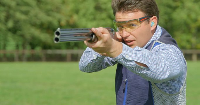 A clay Pigeon Shooter swings double barrel shotgun past camera and pulls the trigger in slow motion.
