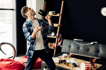 drunk man holding bottle and singing in messy living room after party