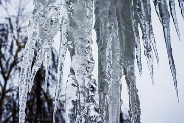 Obraz premium A huge icicle hangs from the roof of the building. Concept: a sign of a close spring and a threat to the life of passers-by.