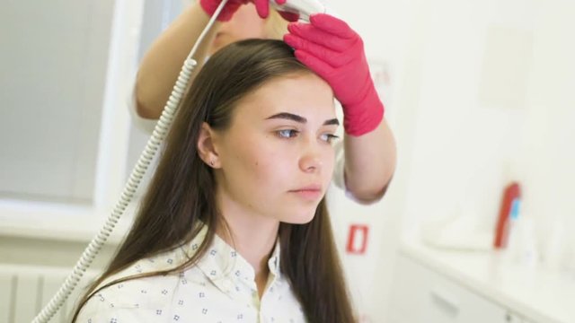 doctor dermatologist diagnoses the structure of the hair of a young pretty girl with a special tool - a trichoscope. Trichology, trichogram