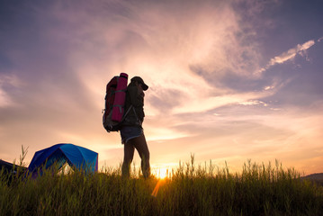 Silhouette Young Woman Traveler with backpack relaxing in sunset. Camping relax after adventure, Sun sets on the horizon behind a camper relaxing and lifestyle hiking travel concept.