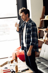 tired man holding glass of water near coffee table with bottles at home