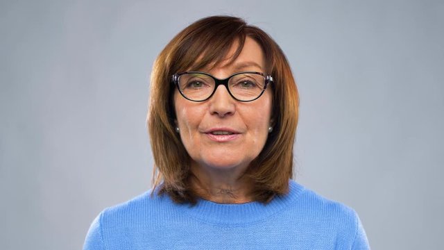 communication, age and people concept - happy senior woman in glasses having video chat or interview over grey background