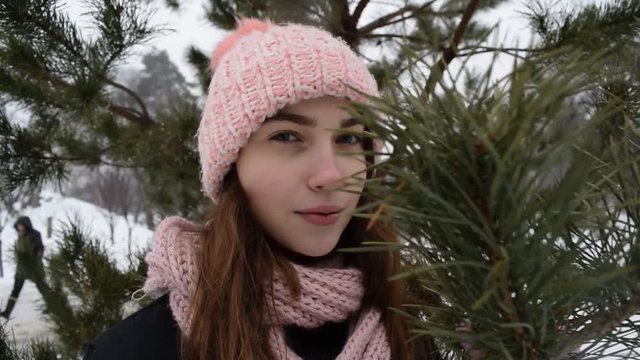View through the branches of a green Christmas tree on the portrait of a girl in a hat in a winter Park.