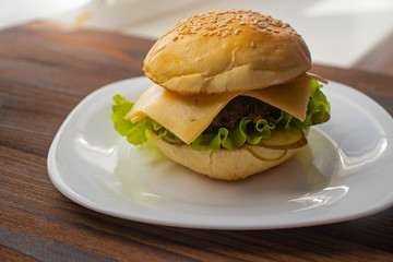 Burger with fried meat patty, cheese and vegetables in a wheat flour bun with sesame seeds.
