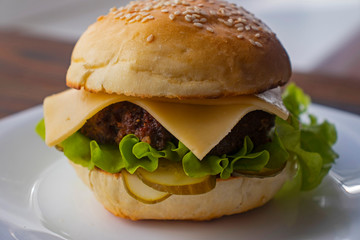 Burger with fried meat patty, cheese and vegetables in a wheat flour bun with sesame seeds.