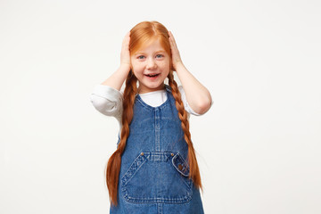 Small naughty red-haired girl broke her mother's favorite vase, standing with her hands over her...