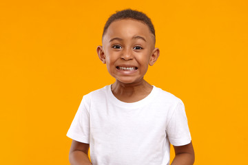 Human emotions, feelings and reaction. Positive emotional dark skinned little boy of 10 year old making funny facial expression, smiling broadly, showing white perfect teeth, posing isolated