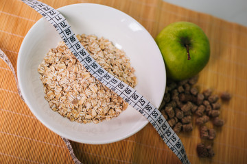 Green apple wrapped by a centimeter. Bran and oatmeal in a plate. Healthy food. Diet for weight loss. Dietary bread