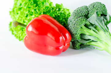 Juicy red pepper with a green tail lies next to Bundle of lettuce and broccoli are on a white...