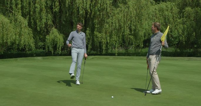 Two brothers /friends playing golf as one just missis the putt and the other laughs!