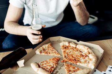 cropped view of man holding bottle near tasty pizza