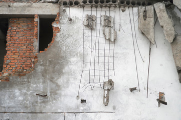 Destroyed white wall with fragments of red brick and concrete stones hanging on the reinforcement....