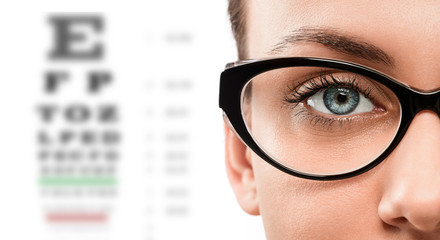 Cloese up of young woman wearing eyeglasses with eyechart in the background