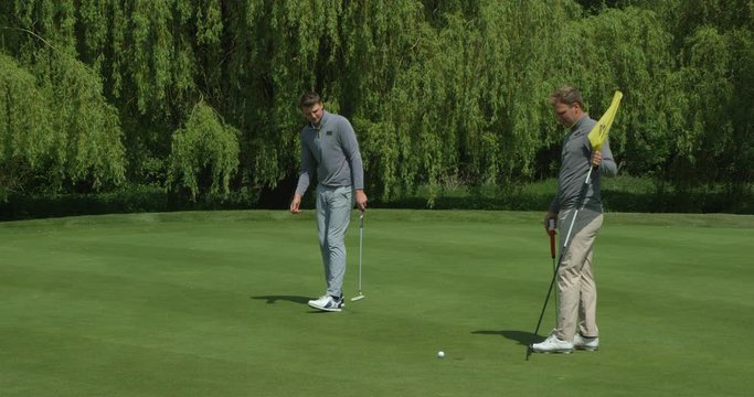 Two brothers playing golf, one narrowly misses the putt the other looks on in enjoyment!
