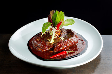 Meat with hot pepper sauce laid out on a white plate.