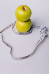 A green apple wrapped with a centimeter lies on a white table. Apple diet
