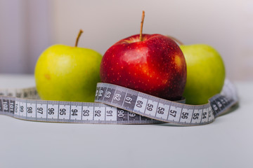 Three red and green apples wrapped with a centimeter lie on a white table. Apple diet.