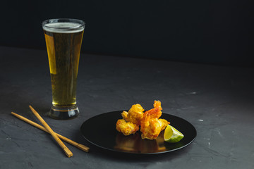Shrimps tempura with lime in black plate and glass of light beer
