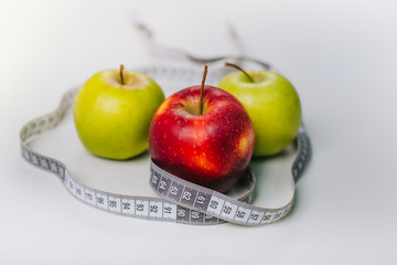 Three red and green apples wrapped with a centimeter lie on a white table. Apple diet.