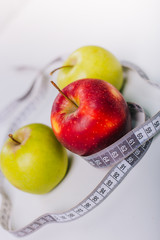 Three red and green apples wrapped with a centimeter lie on a white table. Apple diet.