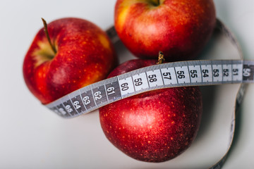 Red apple wrapped centimeter lies on a white table. Apple diet