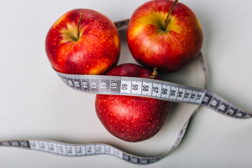 Red apple wrapped centimeter lies on a white table. Apple diet