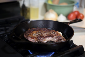 Fototapeta premium Ribeye steak frying in a cast iron pan on a natural gas stove top..