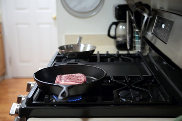 Ribeye steak frying in a cast iron pan on a natural gas stove top.