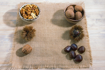 Raw chestnuts in shells, roasted chestnuts, whole walnuts and walnut kernels in a small bowl on a rustic background