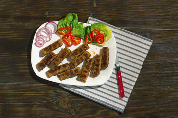 Balkan cuisine. Cevapi - grilled dish of minced meat- with vegetables. Dark rustic background. Flat lay