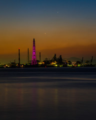 大煙突のある夕方の工場夜景と波間の輝き