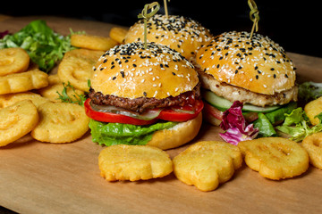 Three hamburger on a board, fries are scattered around.