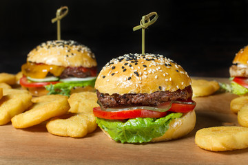 Three hamburger on a board, fries are scattered around.