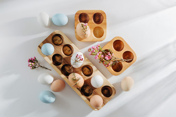 Natural Colored Eggs in wooden egg box and flowers with sunlights. Stylish Compositions in pastel colors.  Eco concept.