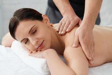 Young beautiful woman enjoying a back massage. Professional massage therapist is treating a female patient in apartment. Relaxation, beauty, body and face treatment concept. Home massage.