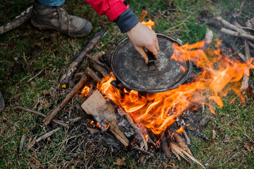 Boy placing a cover on the black pan standing on the bonfire