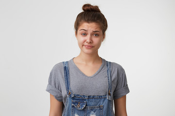 Close up face of a young girl with hair gathered in a bun wears denim overall, look skeptical with...