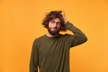 Portrait of bearded casually dressed man in glasses with dark curly hair looking at the camera with...