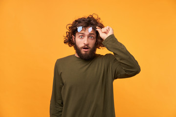 Student saw something unusual, curious, incredible, and even raised his glasses. Bearded curly-haired man raised his glasses looking at the camera his mouth opened in surprise